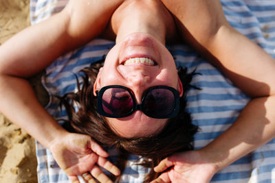 Upper view of woman smiling in the sunglasses lying on striped towel on the beach on a sunny day