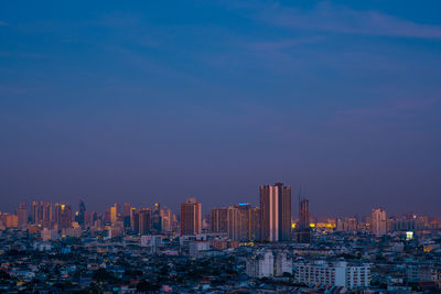 Illuminated buildings in city against blue sky