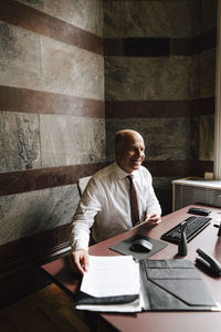 Smiling working senior male financial advisor sitting with document at law office