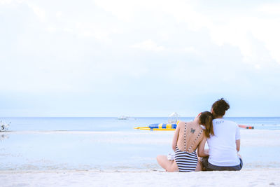 Rear view of siblings relaxing on beach