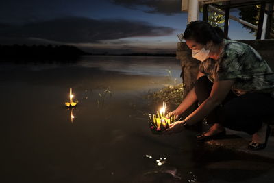 Side view of woman sitting by illuminated candle