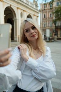 Portrait of woman standing in front of building and making selfie 