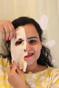 Close-up portrait of smiling young woman removing facial mask