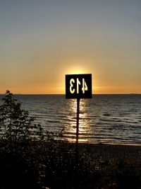 Information sign on beach against sky during sunset