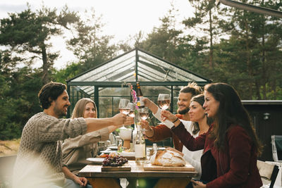 Male and female friends toasting wineglasses while enjoying dinner at garden party