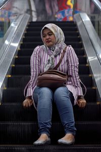 Thoughtful mid adult woman wearing hijab while sitting on escalator