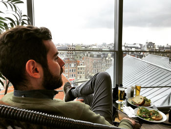 Man looking away while sitting on table by window