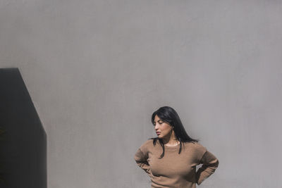 Young woman looking away while standing against wall