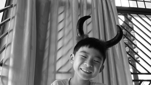 Close-up of boy wearing horns against window at home