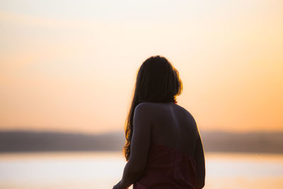 Rear view of woman standing by sea against sky during sunset