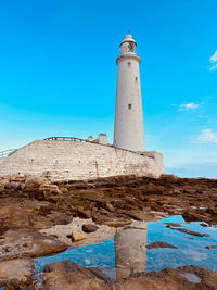 Lighthouse by sea against clear blue sky