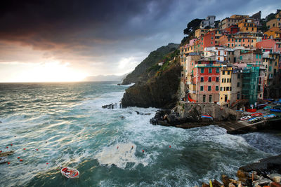 Scenic view of sea by cinque terre against cloudy sky at sunset