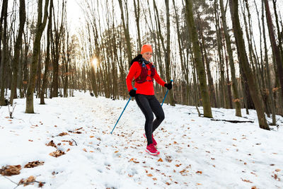 Smiling female runner running down hill with trekking poles on cold winter day.