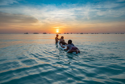 People in sea against sky during sunset