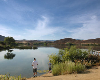 Father and son fishing at lakeshore against sky