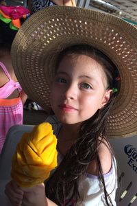 Portrait of cute smiling girl wearing hat while holding mango