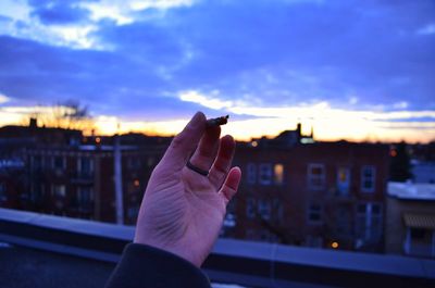 Person holding umbrella against buildings in city at sunset