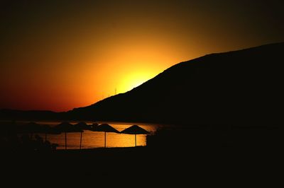 Silhouette mountain by sea against romantic sky at sunset