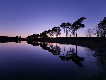 Reflection of silhouette trees in lake against sky