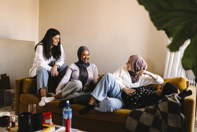 Smiling young women talking with each other while sitting on sofa in living room at home