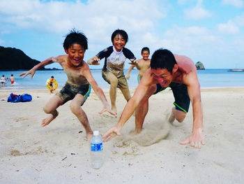 Full length of friends enjoying at beach against sky