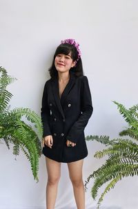 Portrait of smiling young woman wearing black suits standing against plants over white background 