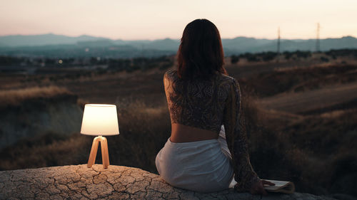 Girl thinks about the future from a rock at sunset with lamp