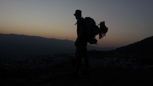 Silhouette male hiker standing with backpack on mountain against clear sky