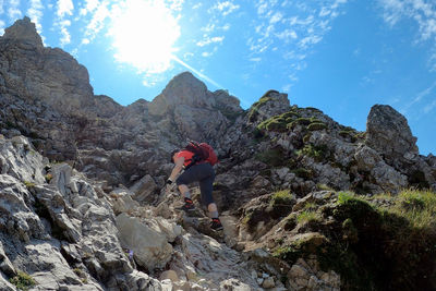 Woman climbing on rock by mountain against sky