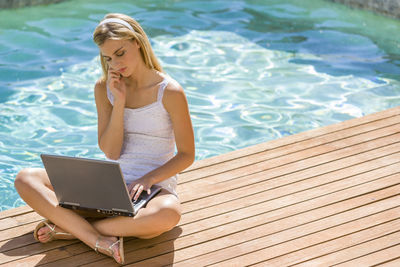 Young woman using laptop while sitting at poolside