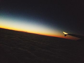 Airplane flying over landscape against sky during sunset
