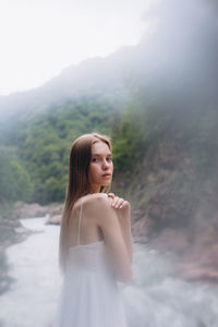 Side view portrait of young woman standing against river