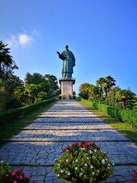 Statue on footpath against blue sky