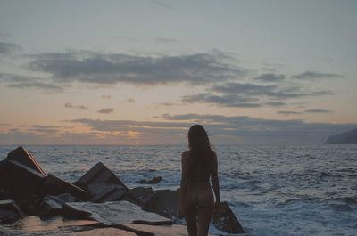 Woman standing on beach against sky during sunset