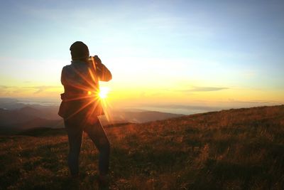 Rear view of man standing on field against sky during sunset