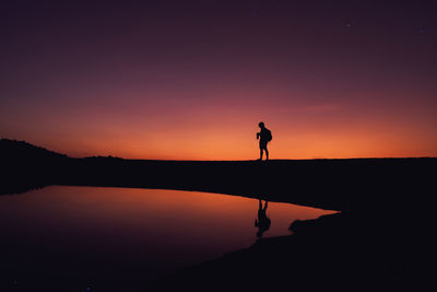 Silhouette man standing by lake against sky during sunset