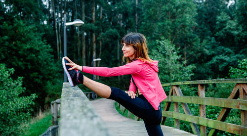 Smiling athlete woman doing leg stretch outdoors