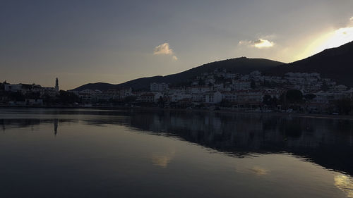Scenic view of lake by buildings against sky during sunset
