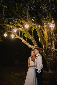 Woman standing by illuminated tree at night