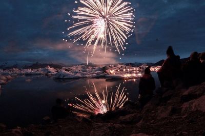 People by lake looking at firework display during dusk