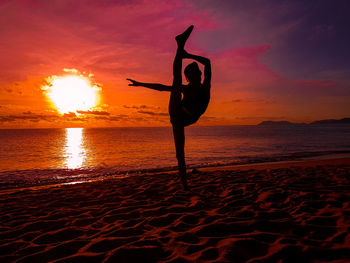 Silhouette girl stretching on sand at beach against sky during sunset