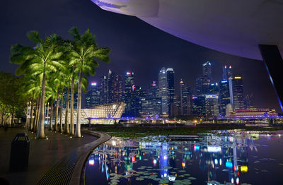 Illuminated modern buildings by city against sky at night