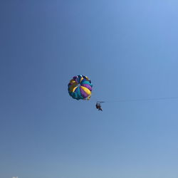 Low angle view of people parasailing against clear blue sky