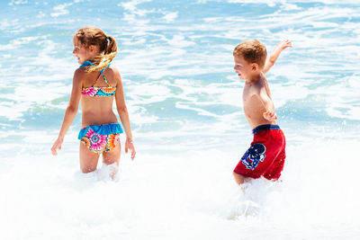 Carefree siblings standing in sea during sunny day