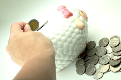 Cropped hand inserting coins in piggy bank on table