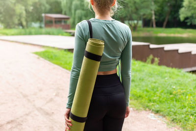Rear view, a woman in the park in summer, with a green gym mat behind her back