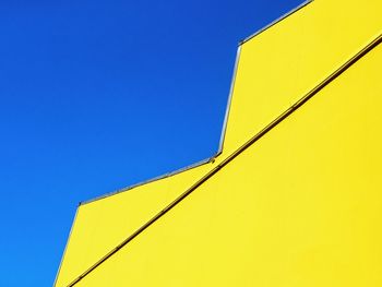 Low angle view of yellow building against clear blue sky