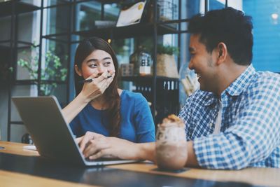 Man and woman using smart phone while sitting on table