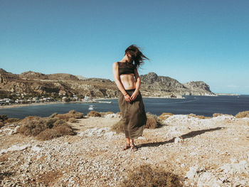 Woman standing on rock at beach against clear sky