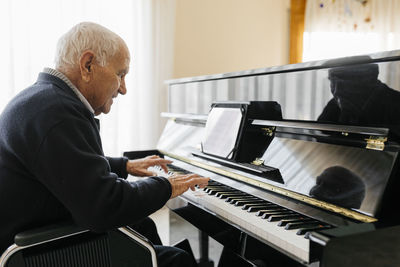 Senior man sitting in wheelchair playing piano at home